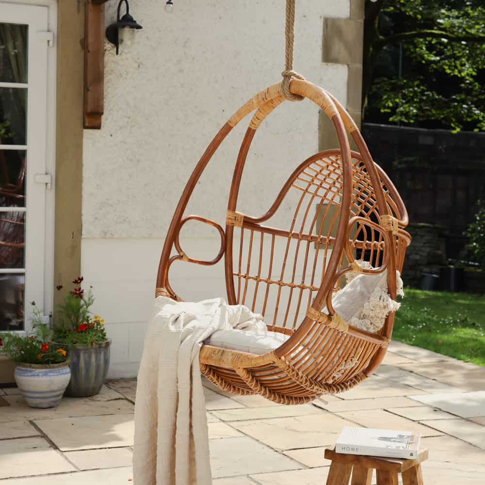 Rattan garden hanging egg swing chair with throw and cushion draped over.