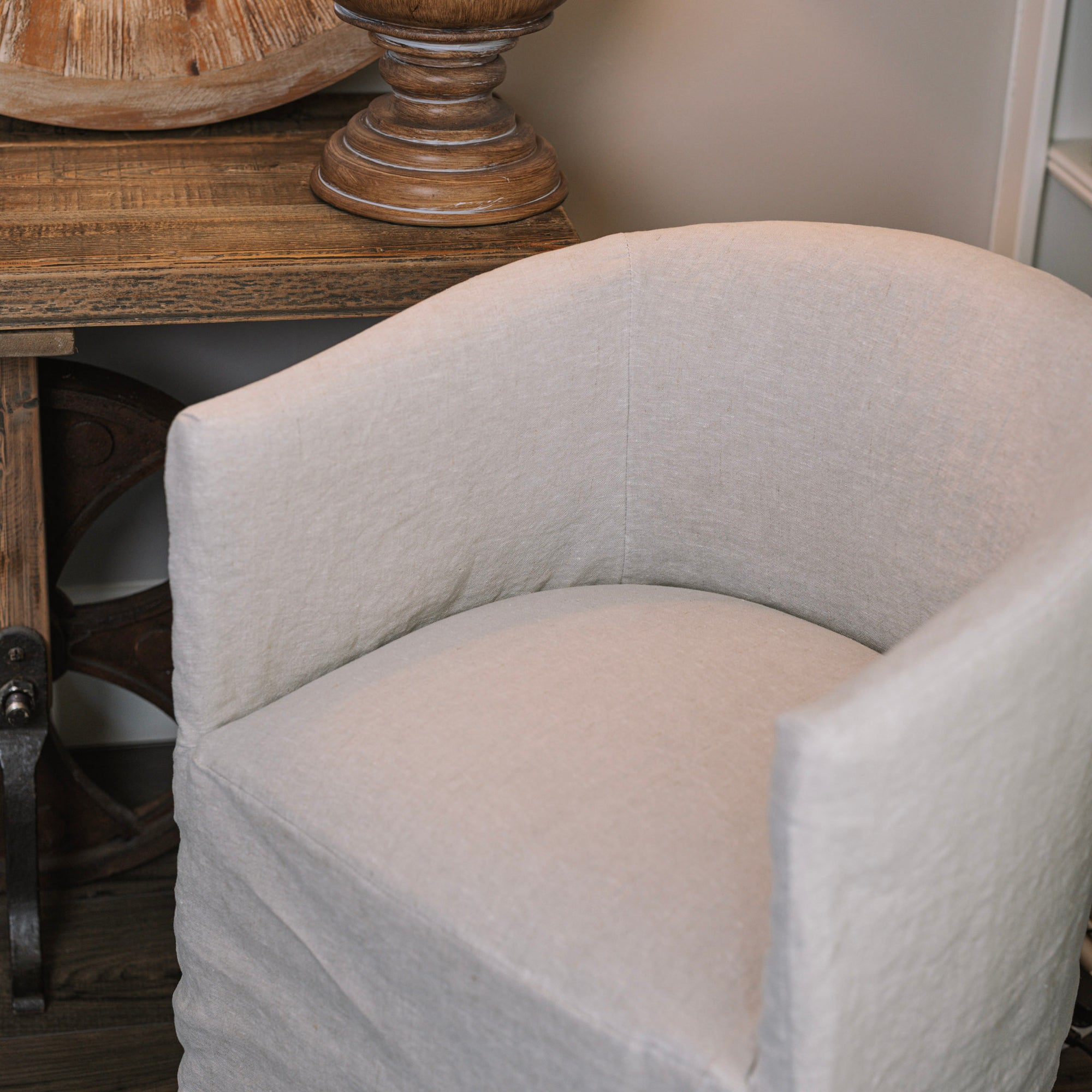 close up image of Natural linen dining chair with rounded back next to a wooden side table.