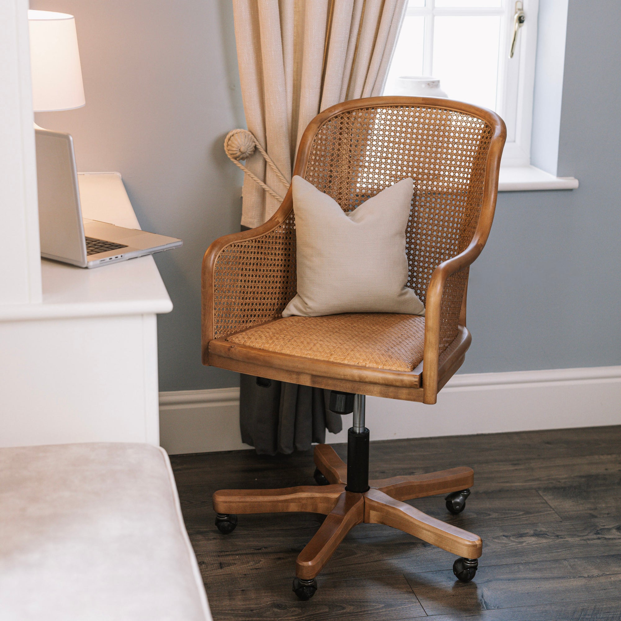 Natural rattan wicker office chair with neutral cushion at white desk.