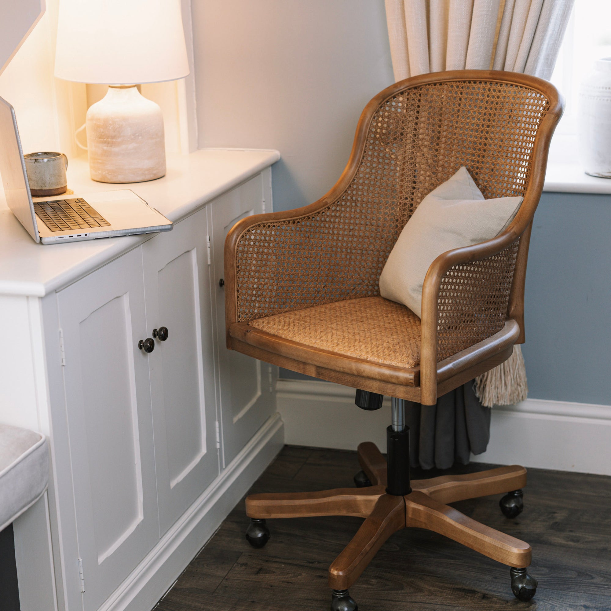 Natural rattan wicker office chair with neutral cushion at white desk.