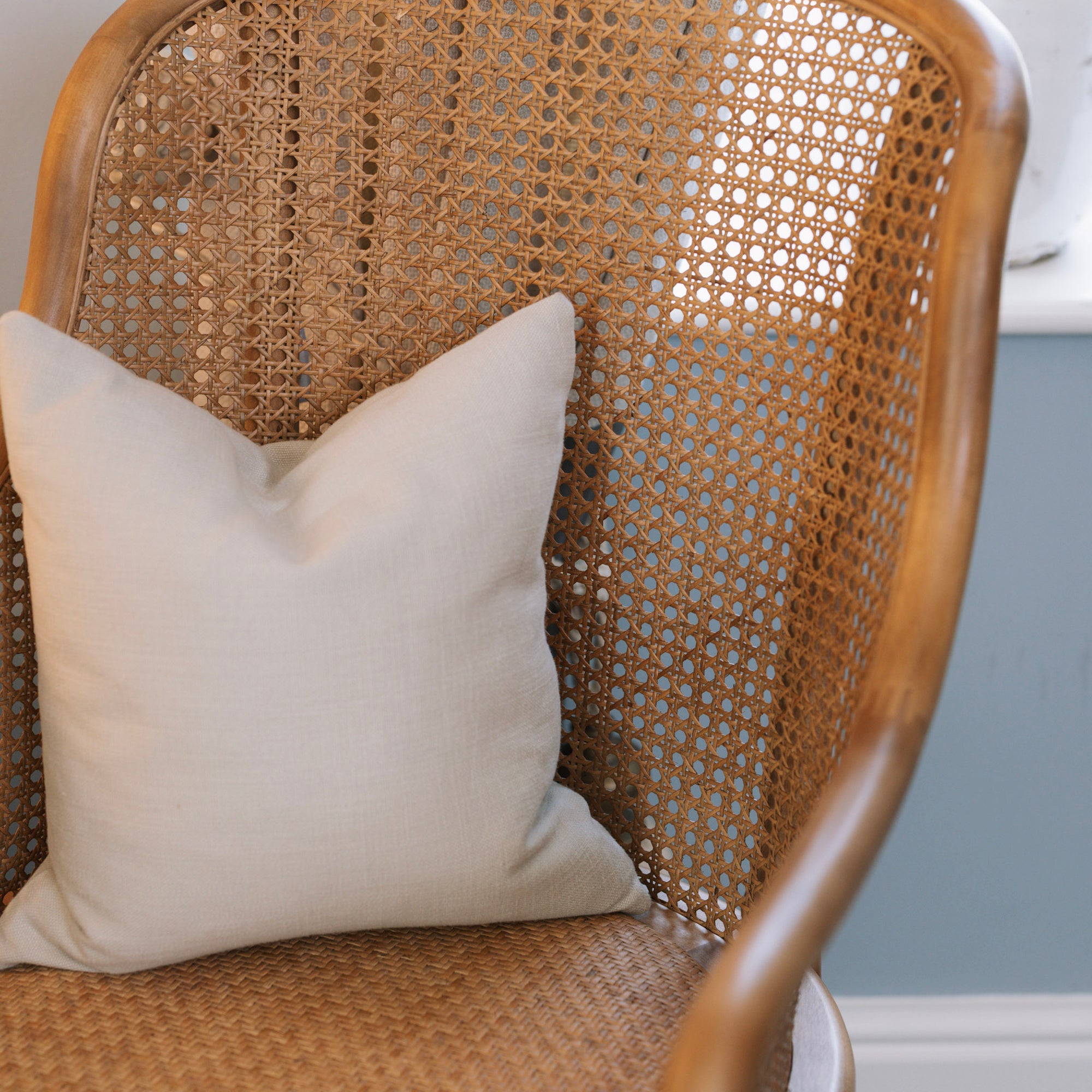 Natural rattan wicker office chair with neutral cushion at white desk.