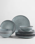 Blue hued striped 12 piece dinner set, stacked up on white background.