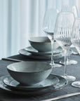 Styled dinner table with wine glasses, blue dinnerware stacked up and cutlery.