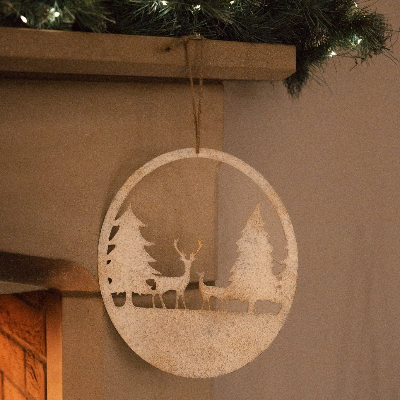 Reindeer scene hanging decoration, hanging from a fireplace mantel with a garland.