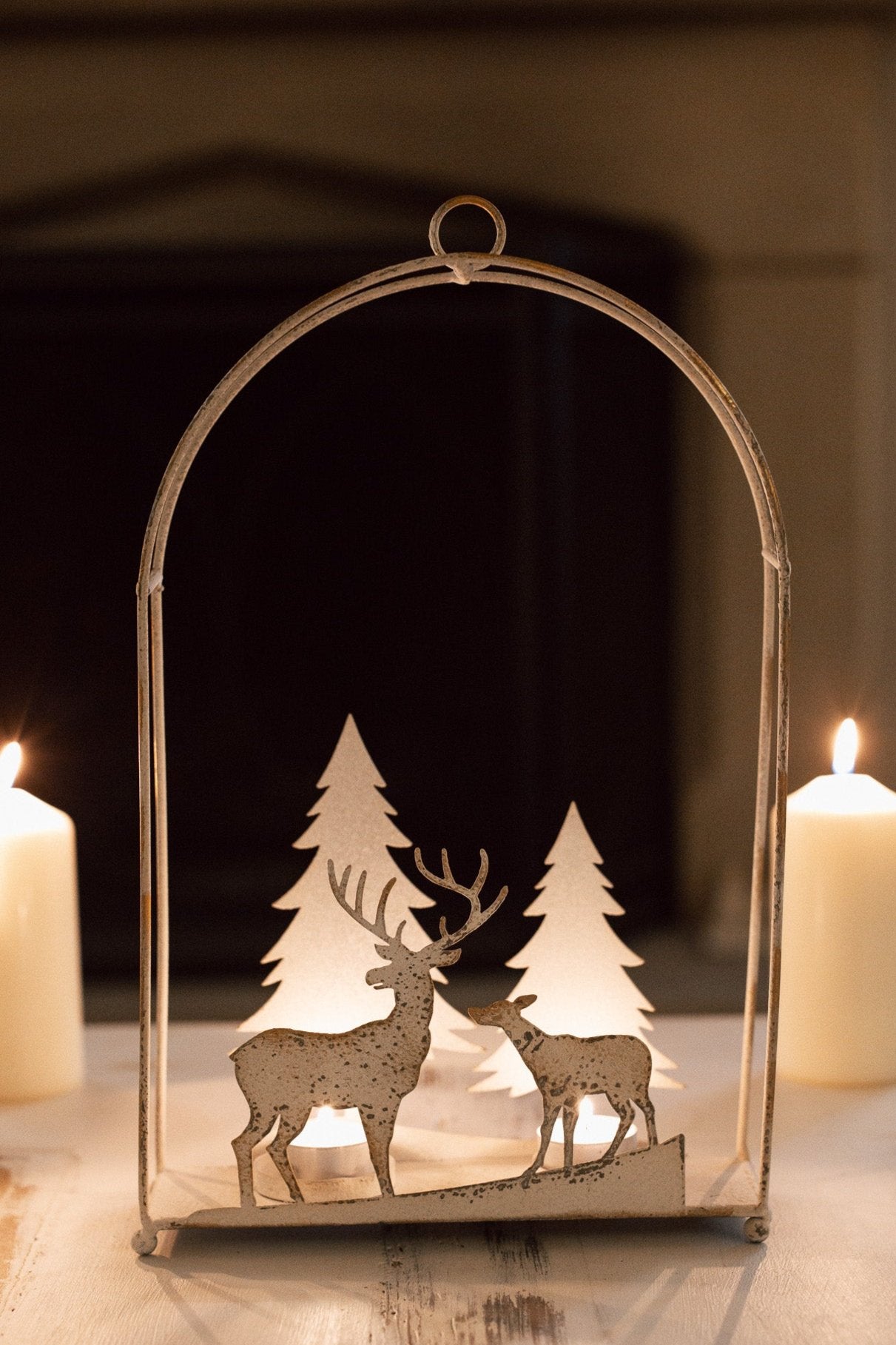 White reindeer forest scene hanging wall decor with lit tealights in, on a table with dinner candles behind.