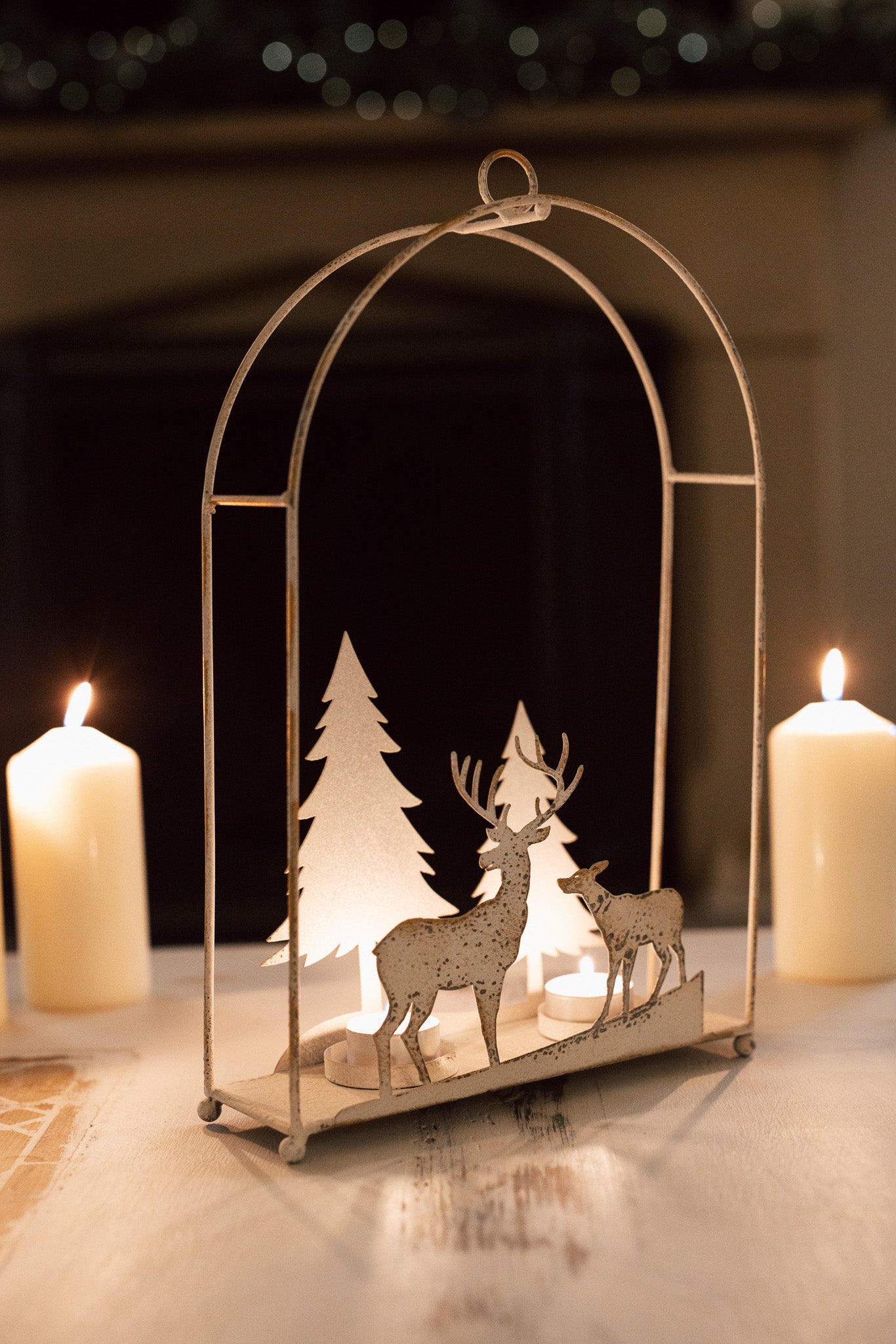 White reindeer forest scene hanging wall decor with lit tealights in, on a table with dinner candles behind.