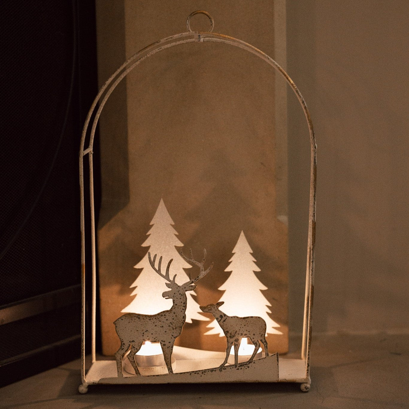 White reindeer forest scene hanging wall decor with lit tealights in, on a fireplace hearth.