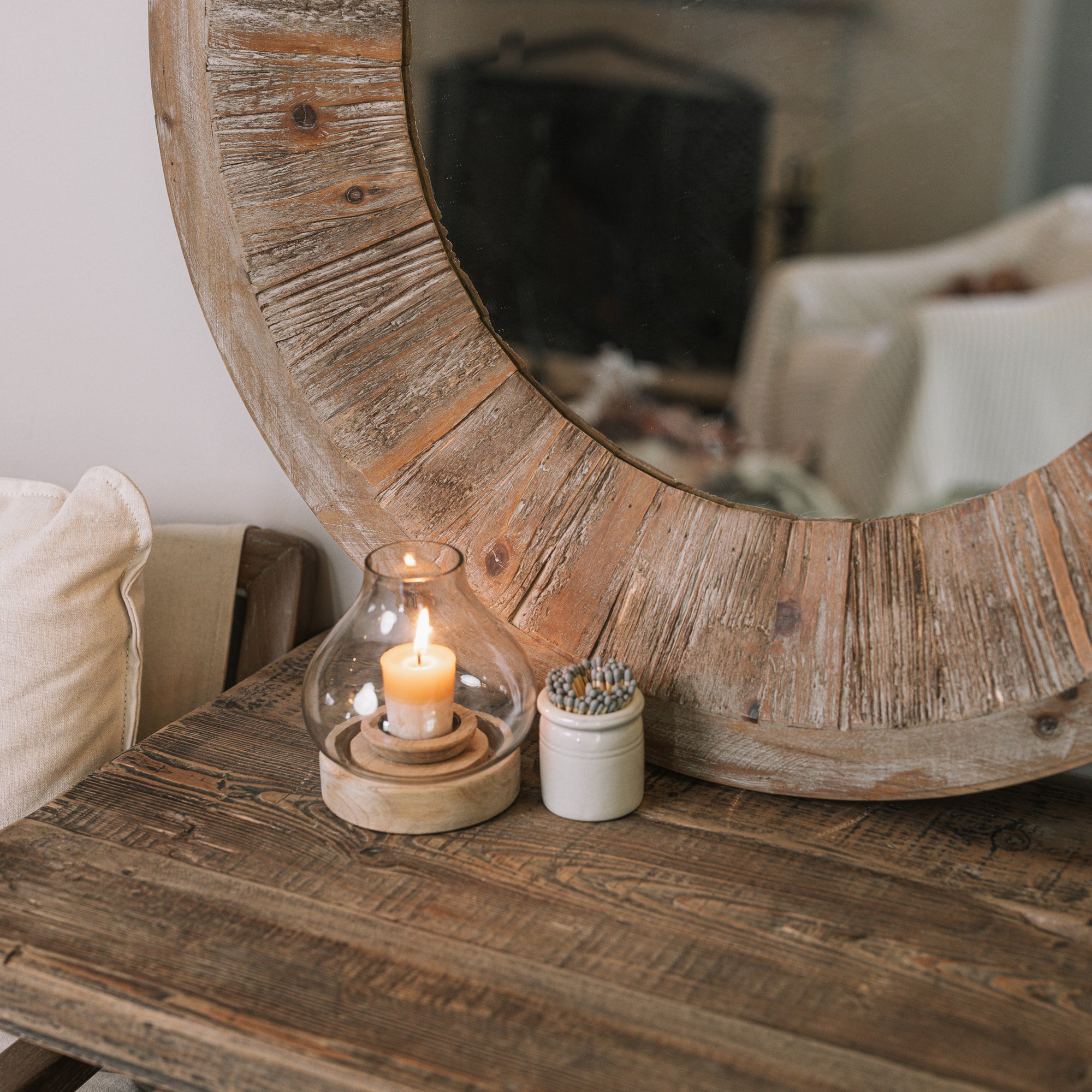 Rustic Round Wooden Mirror on wooden table with small candle and pot of matches.