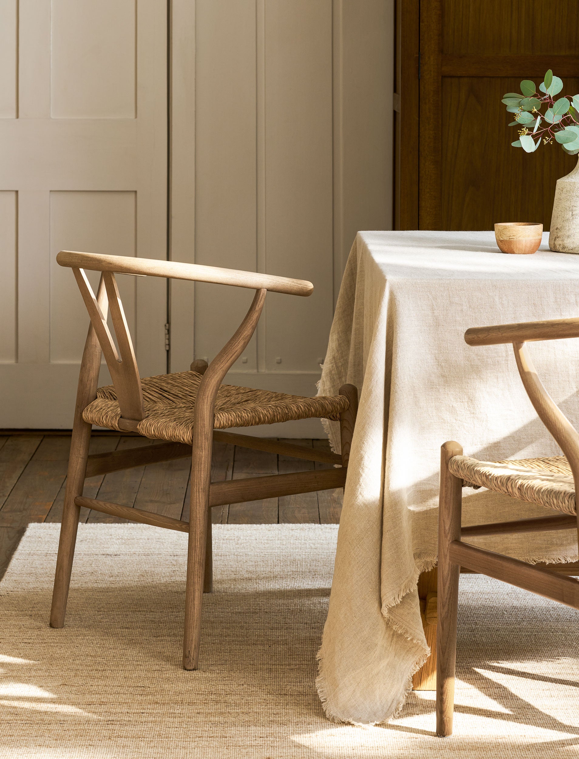 Dining room with wishbone dining chairs and a table covered with a beige tablecloth.