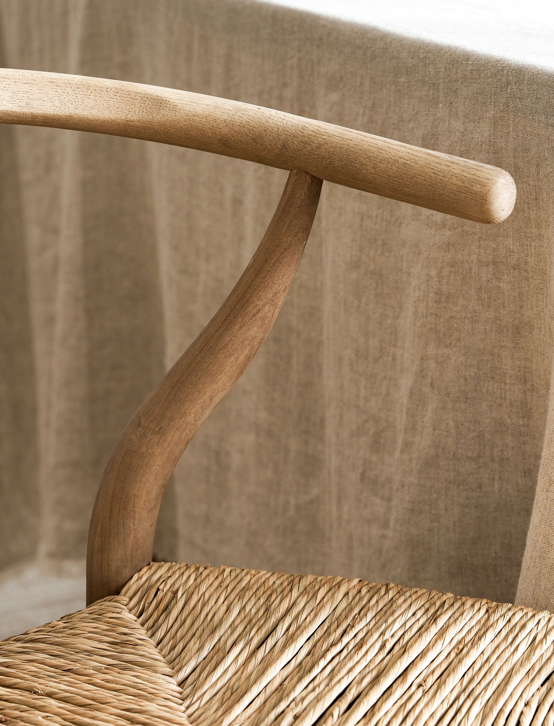 Close-up of a wooden wishbone dining chairs with wicker seat against a neutral background