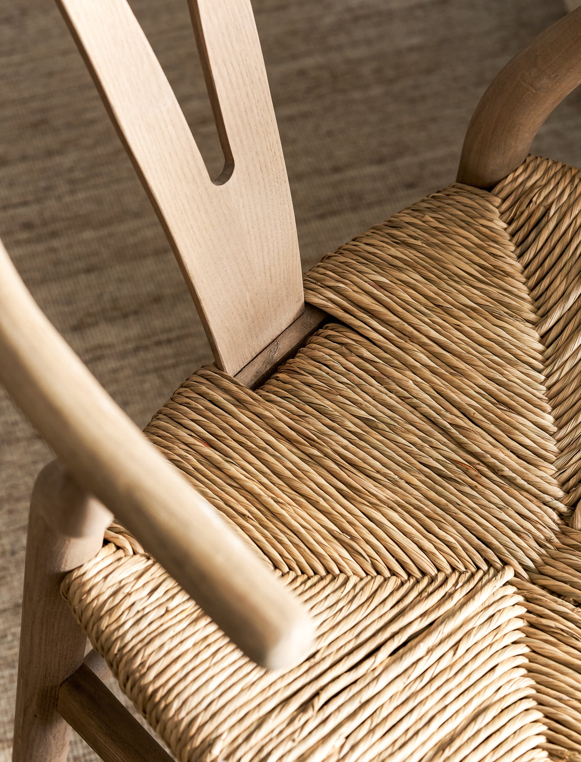 Close-up of a wooden wishbone dining chairs with woven seat and backrest.