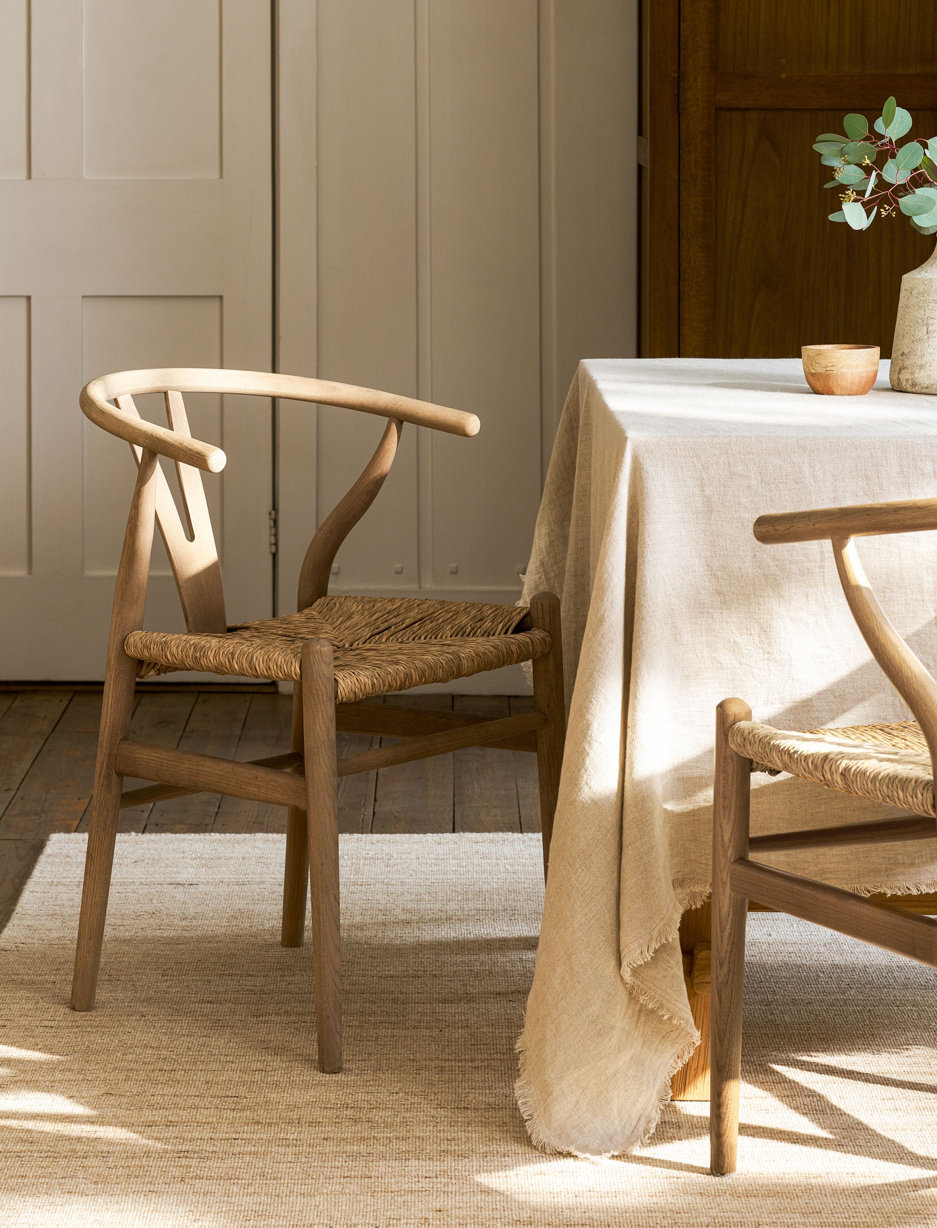 Dining room with wishbone dining chairs and a table covered with a beige tablecloth.