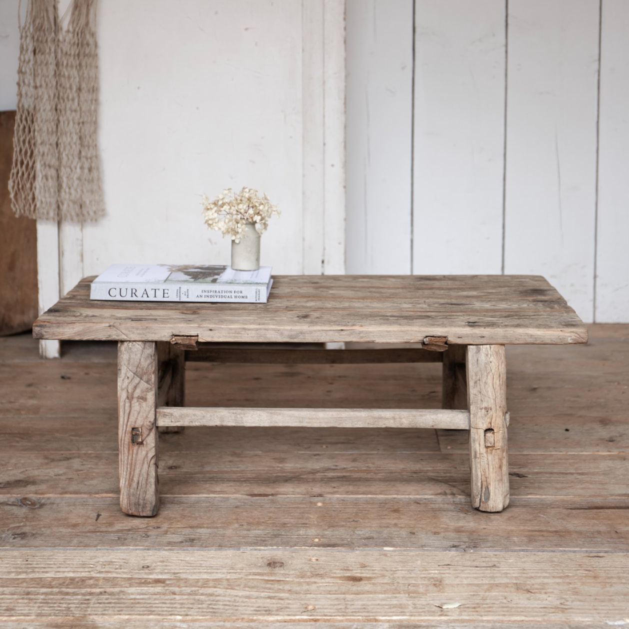 A Reclaimed Wood Coffee Table against a rustic white wooden wall.