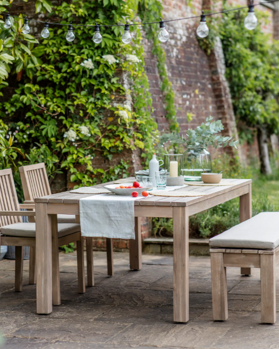 Outdoor dining table with chairs and benches, and crockery on top.