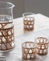 3 glass tumblers with a large glass jug aside on a table with natural table cloth.