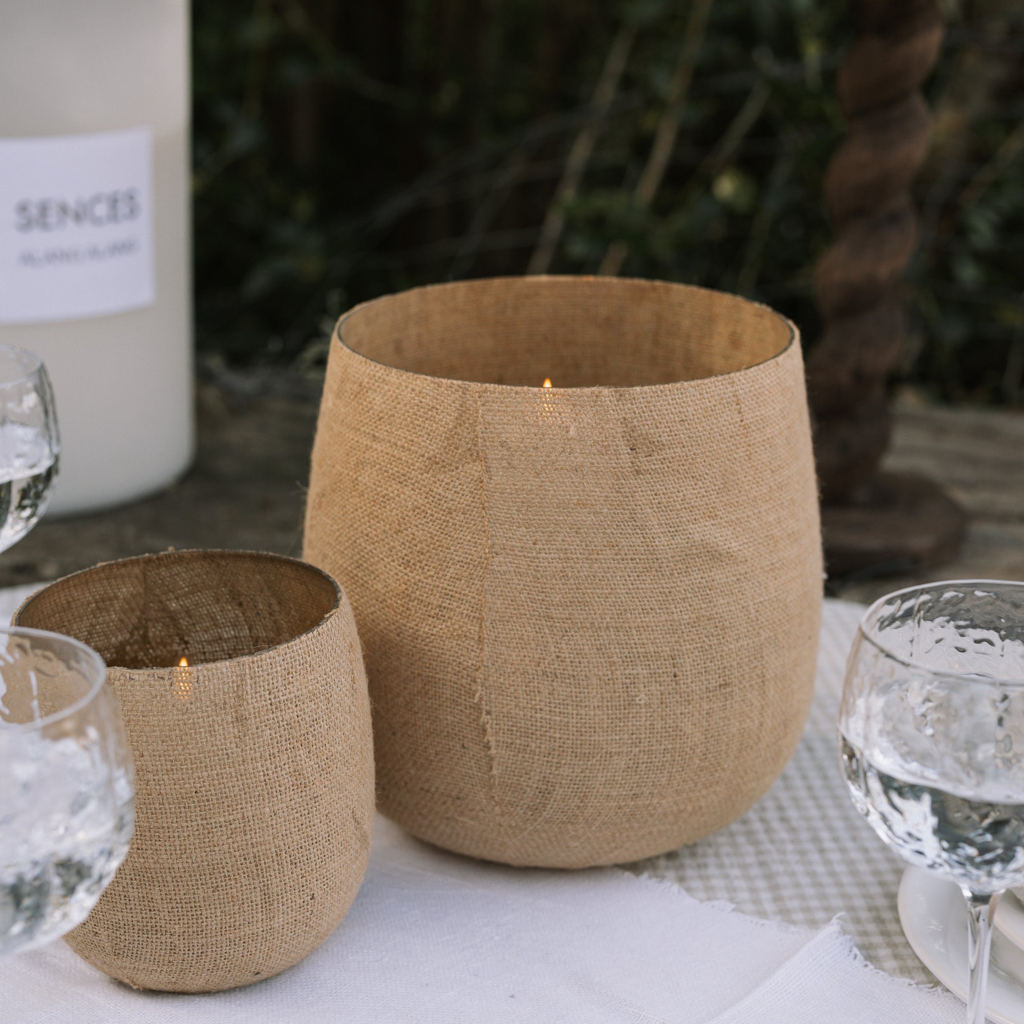 Set of two Jute Hurricane Lantern on linen and gingham table cloth outdoors. 