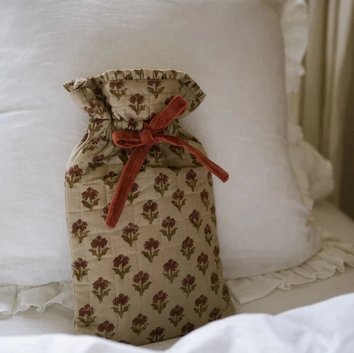 Neutral and red patterned hot water bottle on white bedspread, tied up with a bow.