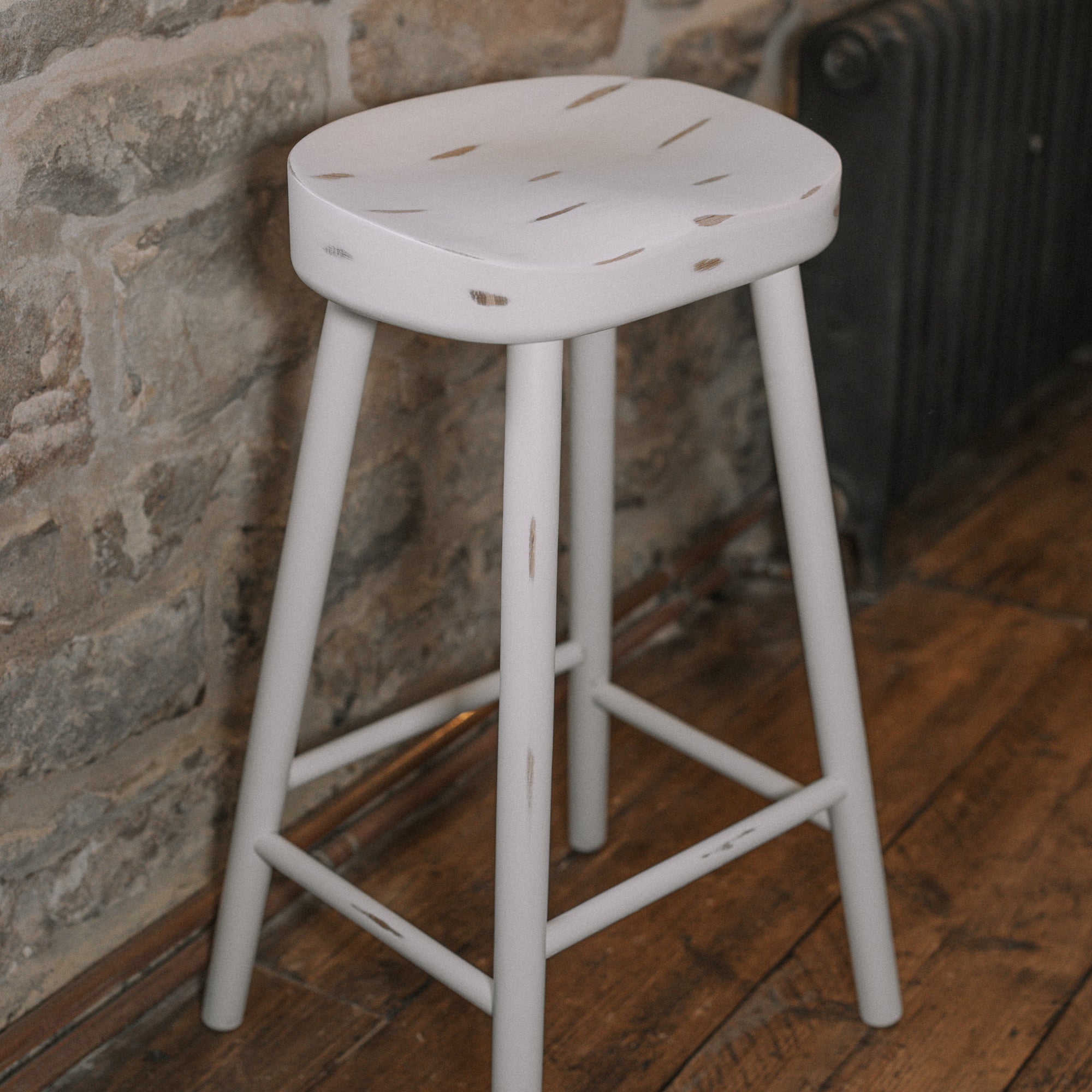 White washed rustic wooden bar stool against stone wall.