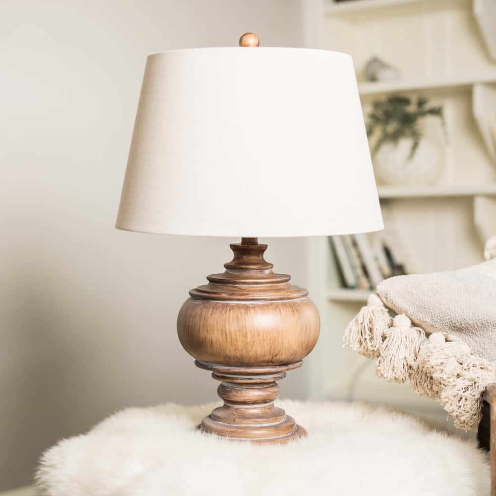 Wooden table lamp with beige linen shade on flurry table.