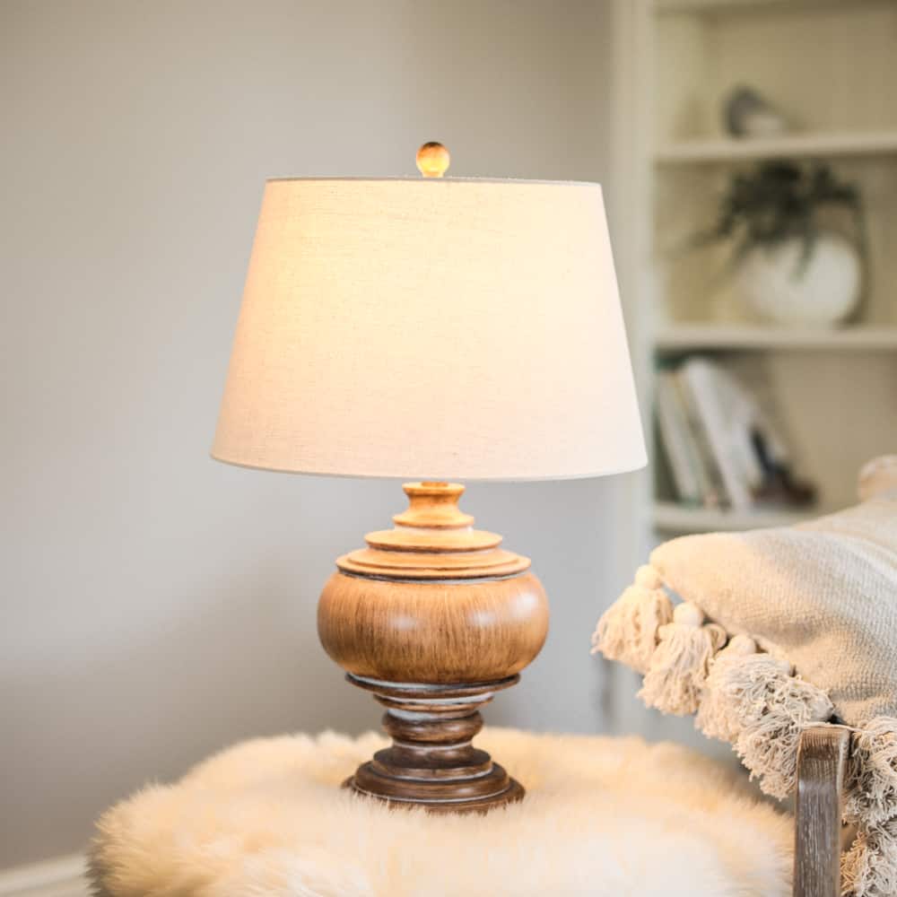 Wooden table lamp with beige linen shade switched on, on flurry table.