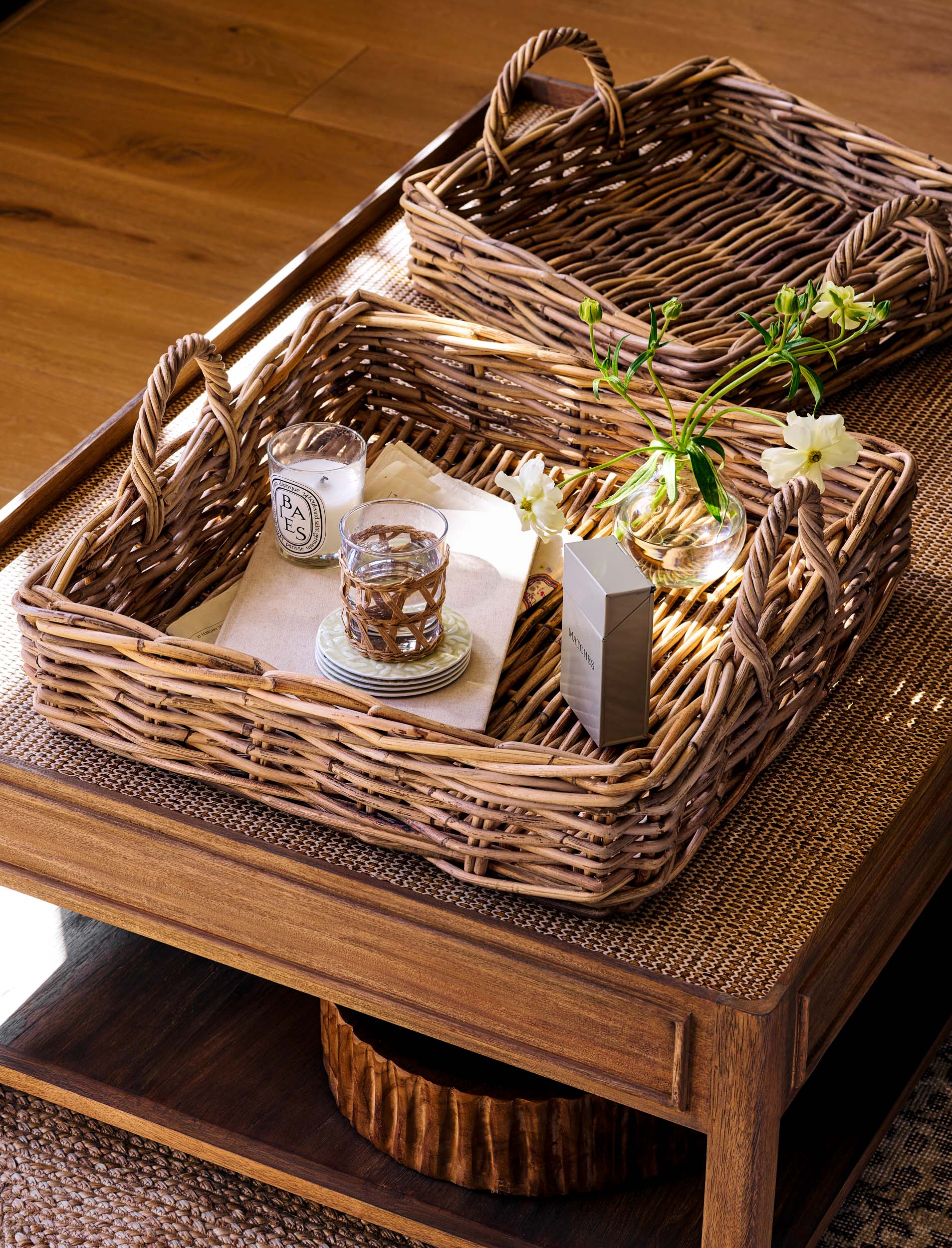 Natural woven trays on a wooden table with a glass of water and a bottle.