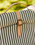 Striped lunch bag with a brown strap and buckle against a blurred green background