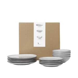 The Broste Copenhagen Nordic Sand 12 piece Dinner Set stacked in front of a cardboard box.