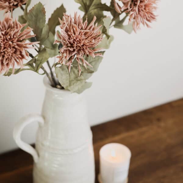 Dusty pink coloured Dahlia flowers in a vintage vase with a candle.