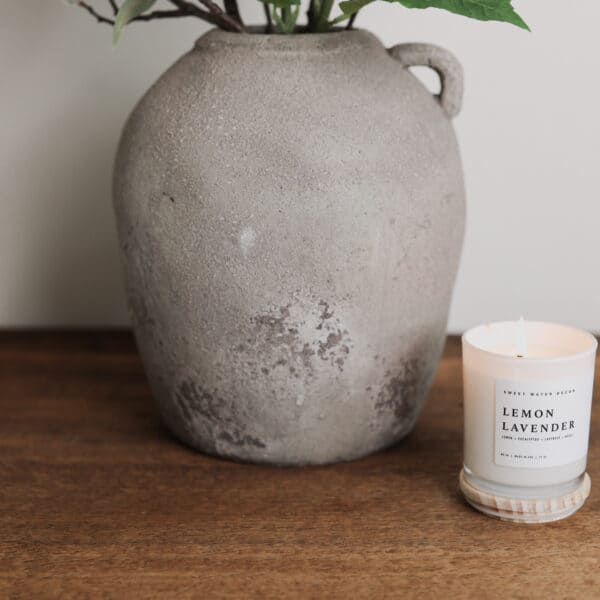a rustic grey vase on a wooden desk with a small scented candle.