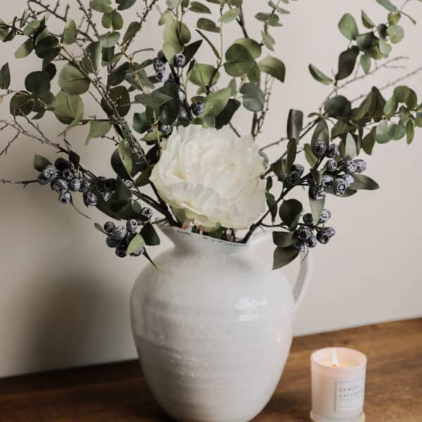 A bouquet of muted tone stems in a speckled vase on a wooden desk.