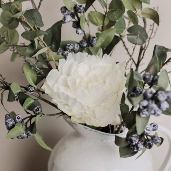 A bouquet of muted tone stems in a speckled vase on a wooden desk.