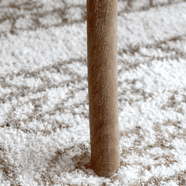 White washed wooden chair leg on a white and beige rug.