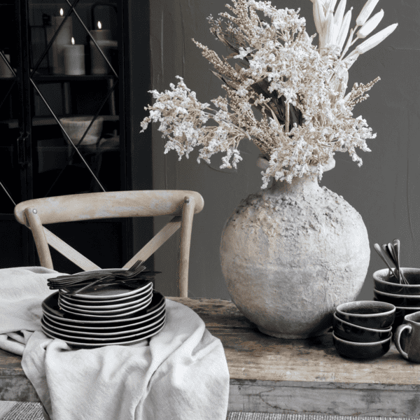 dining table with a rustic stoneware vase and stack of plates.