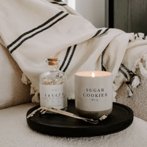 Sweet Water Decor Sugar Cookies Soy Candle In Stoneware Jar on tray on sofa with matches