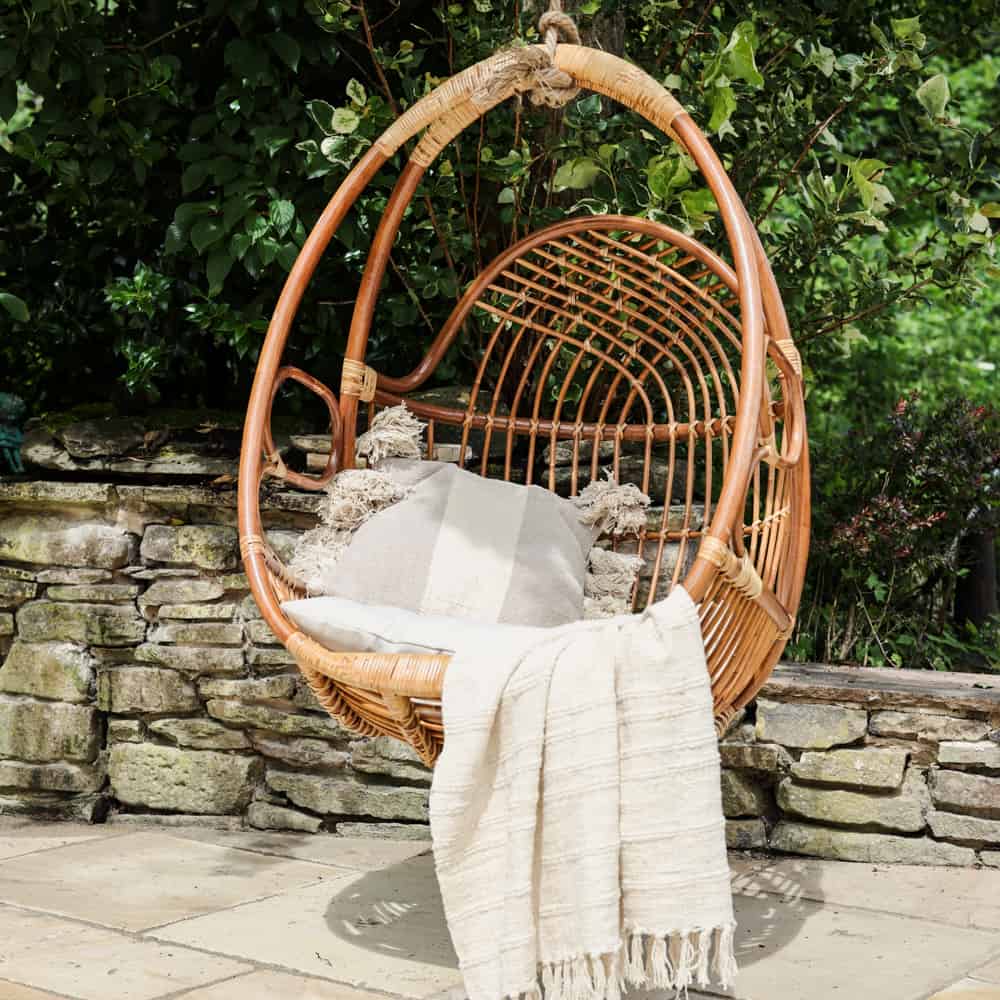 Outdoor hanging egg swing chair with throw and cushion on.
